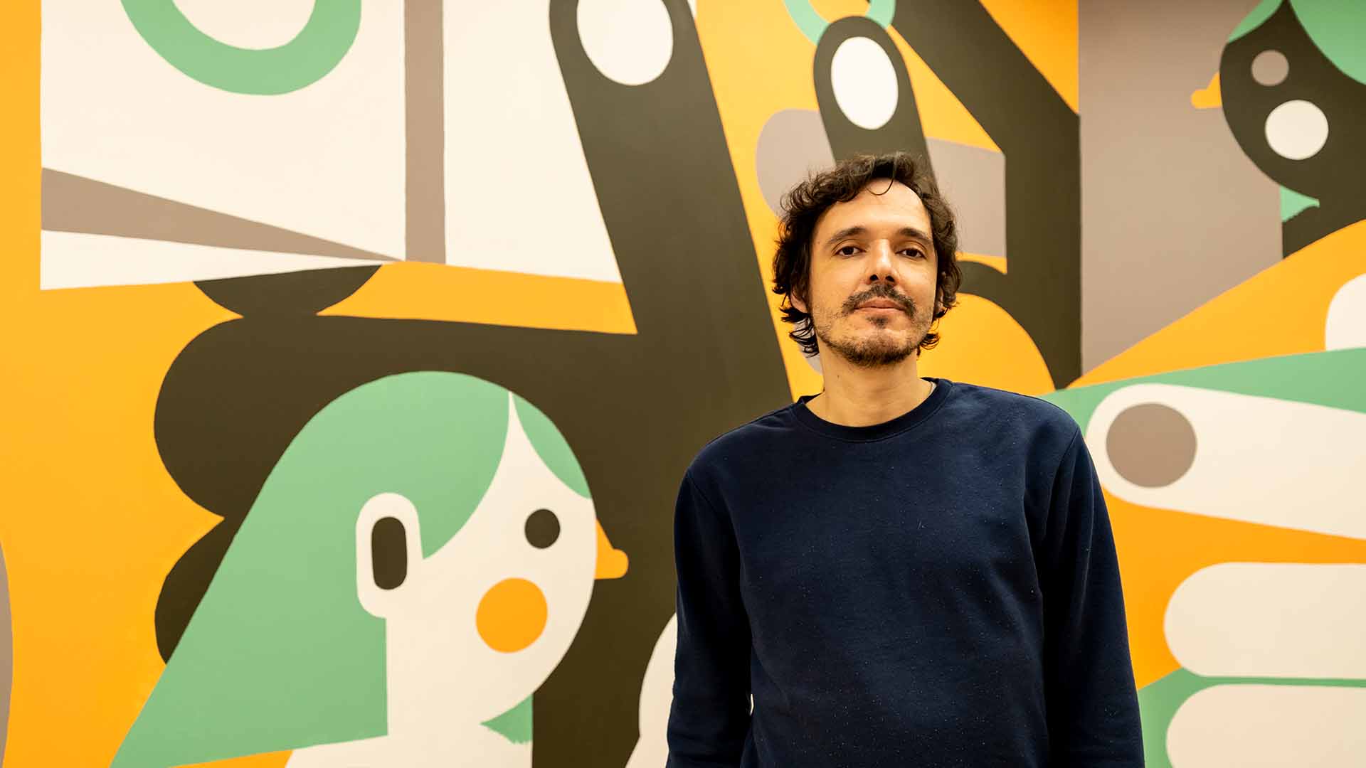 A portrait photo of Tiago Galo standing in front of a wall with his artwork.